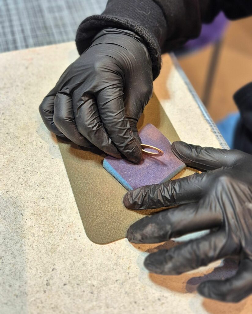 Mains gantées ponçant une pièce de cuivre avant l'émaillage