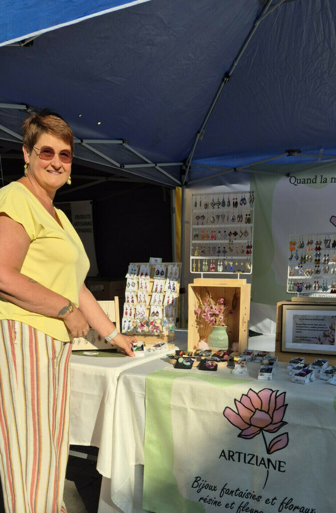 Le stand Artiziane sur un marché : présentoirs de boucles d'oreilles, bouquet de fleurs séchées et banderole Artiziane sous une tonnelle