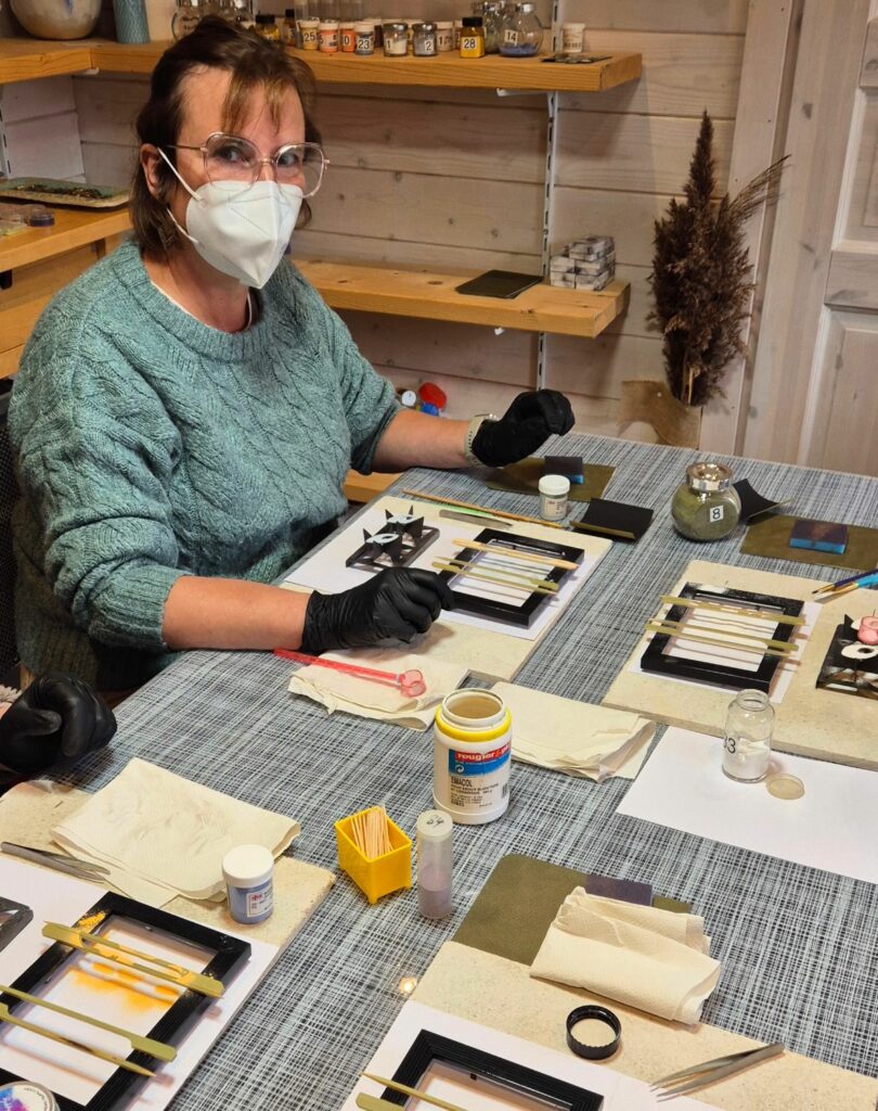 Une participante, gantée et masquée, émaille ses pièces de cuivre à la table de l'atelier