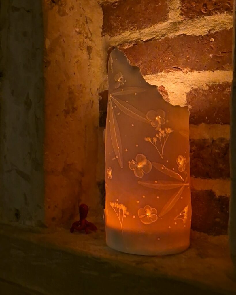 Pièce en céramique aux empreintes de fleurs et de feuilles, éclairée de l'intérieur, posée dans une niche en briques
