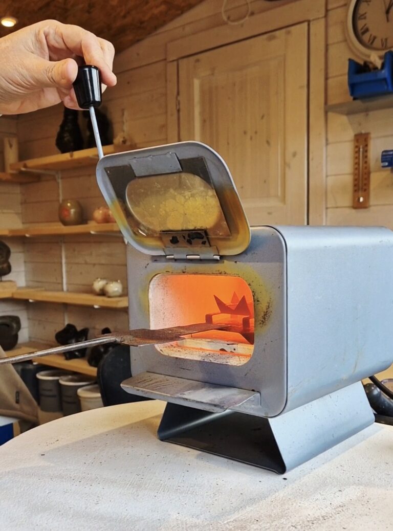 Pièce de cuivre émaillée déposée à la pince dans le four rougeoyant de l'atelier