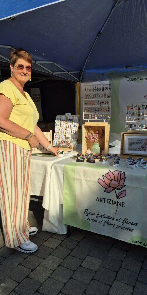 Le stand Artiziane sur un marché : présentoirs de boucles d'oreilles, bouquet de fleurs séchées et banderole Artiziane sous une tonnelle