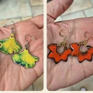 Boucles d'oreilles en émail sur cuivre, feuille de ginkgo jaune et fleurs orange, dans la main
