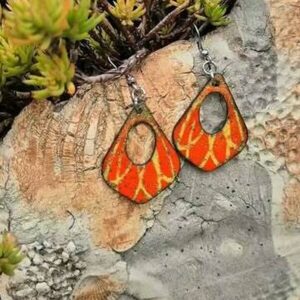 Boucles d'oreilles gouttes ajourées en émail orange veiné de jaune, posées parmi des plantes grasses